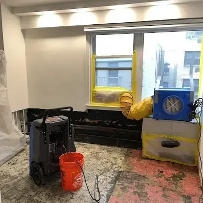 A dehumidifier and an air mover drying a room with the flooring removed