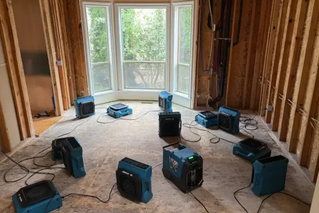 Air movers and dehumidifiers running in a room opened up for drying